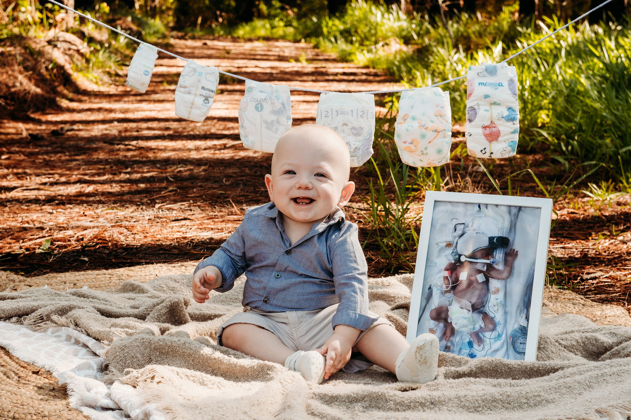 Henry sits with a photo of himself as a newborn, in front of a row of nappies showing his growth from his premature birth to one year old.