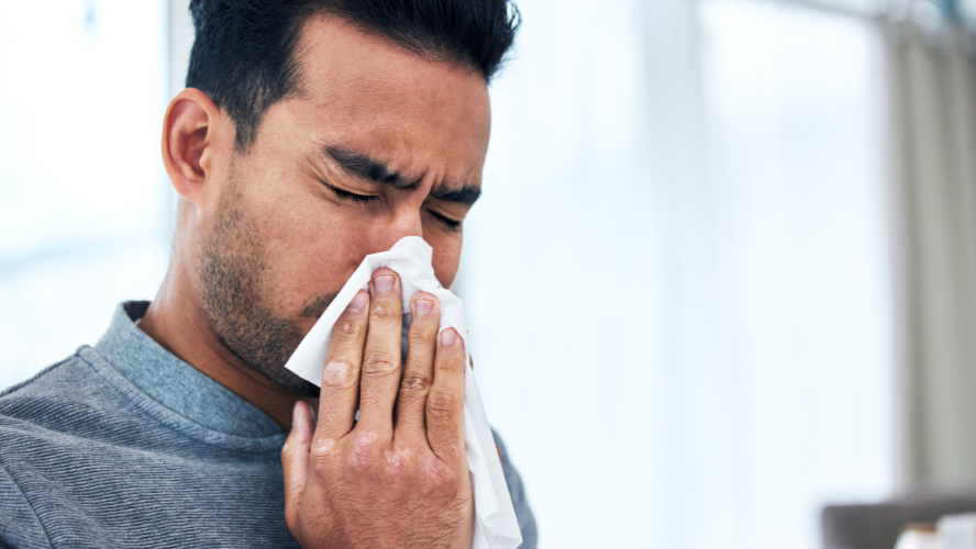 A man blows his nose into a tissue.