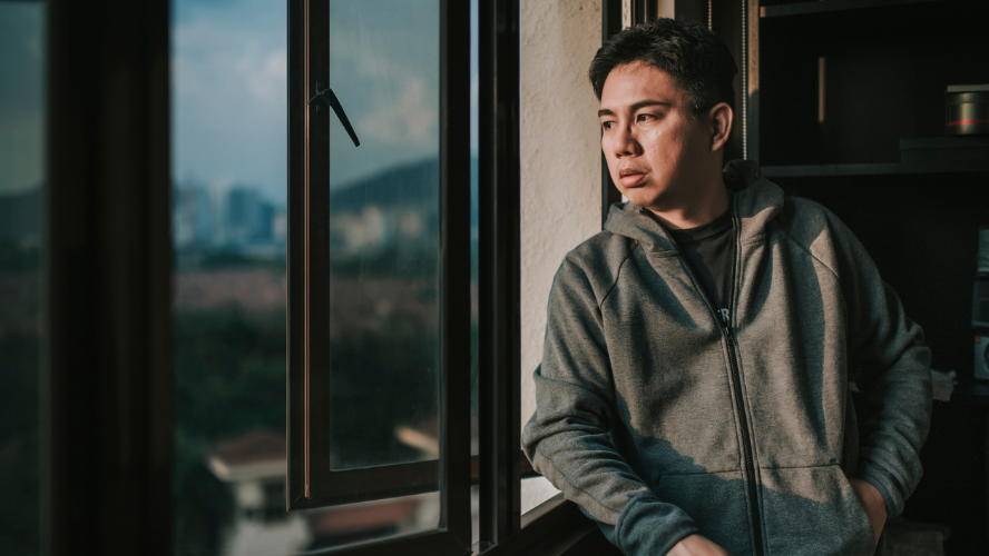 A man stands alone looking out a window.