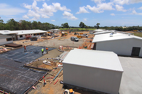 A construction site with a building frame to the left, digging machines in the middle and a person in high vis gear walking across red dirt